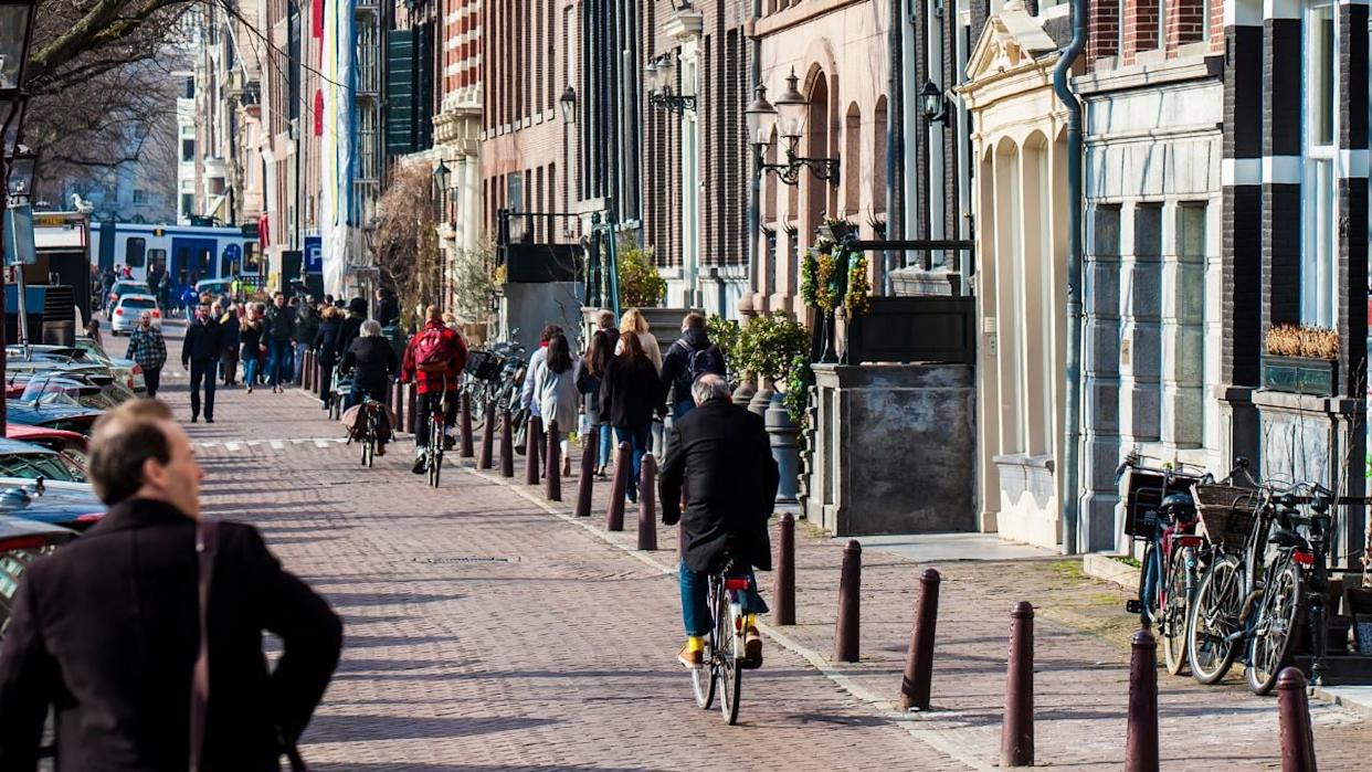 AMSTERDAM, NETHERLANDS - MARCH, 2018: People walking and riding bicycles at the beautiful cobblestone streets next to the canals of the Old Central district of Amsterdam