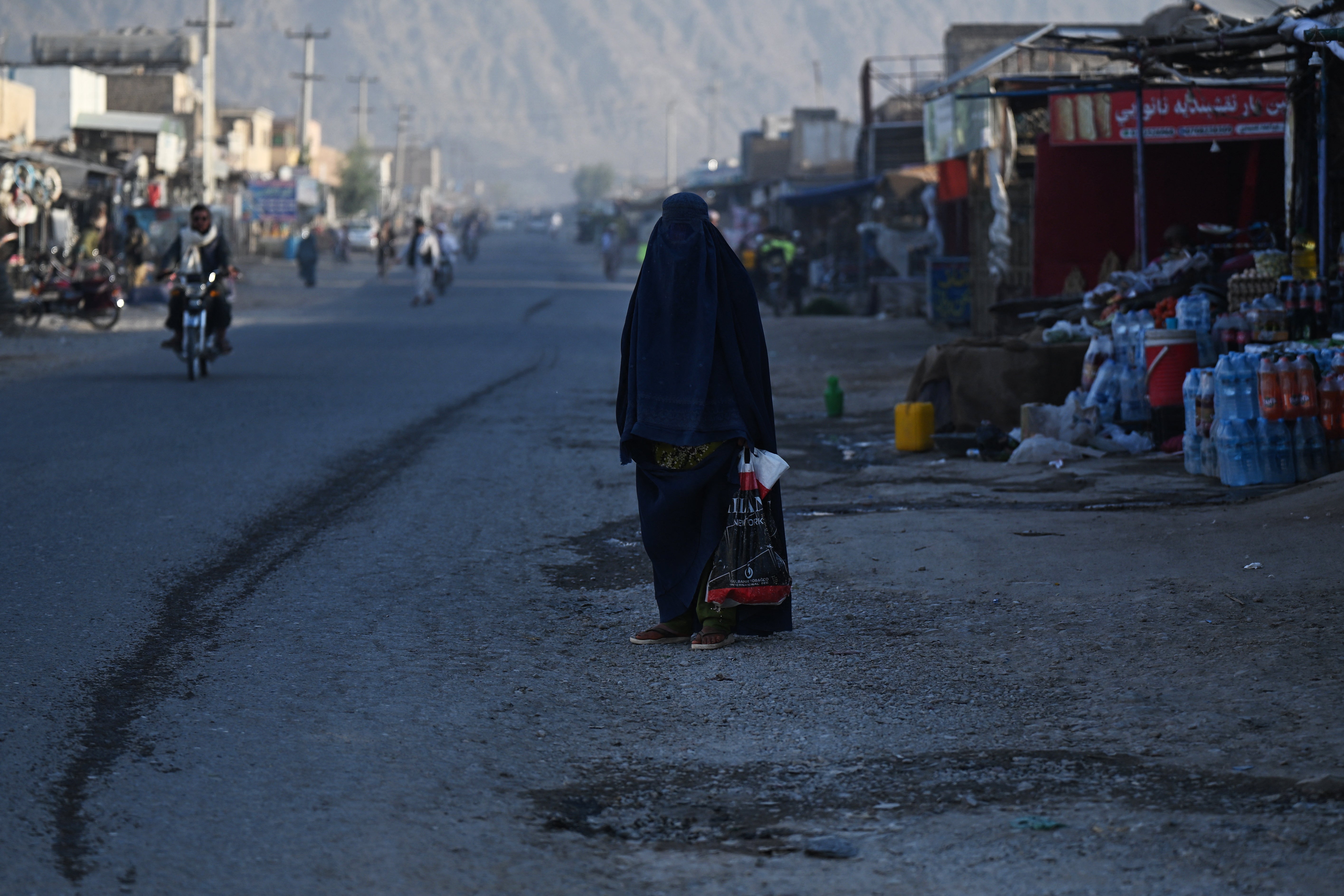 An Afghan burqa-clad woman waits for a taxi along a street at a village in Kandahar