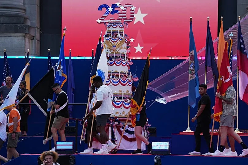 People carry flags past a giant birthday cake to celebrate during the America 250 event in Brussels, Sunday, June 28, 2026. (AP Photo/Virginia Mayo)
