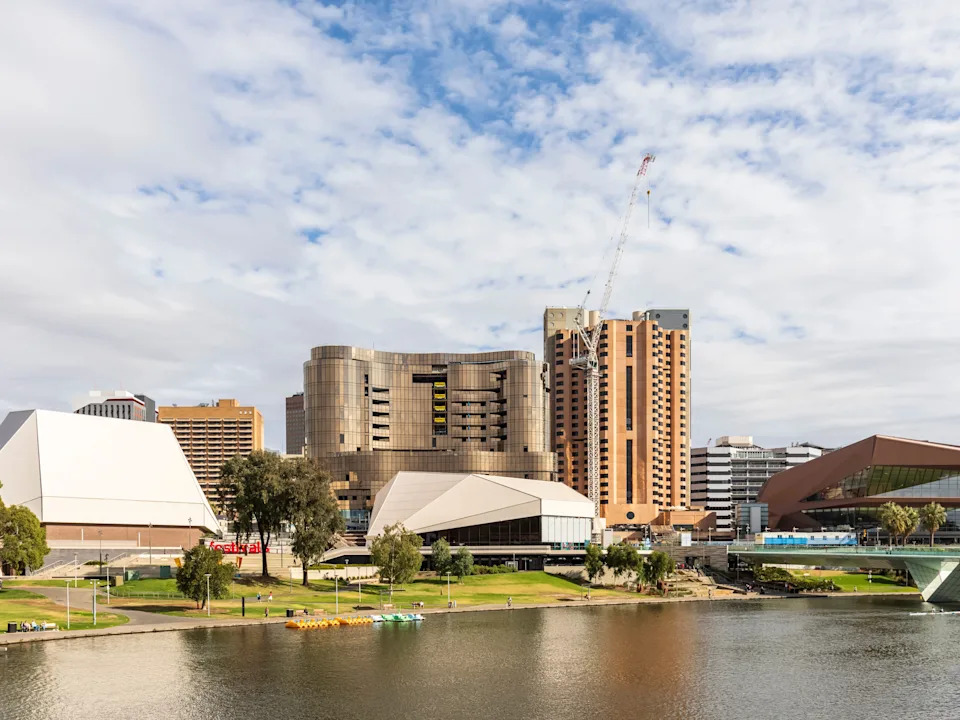 Adelaide riverfront skyline with buildings and a construction crane. A body of water is in the foreground.