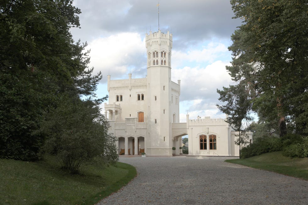 White castle with a tall tower, surrounded by trees and cloudy sky.
