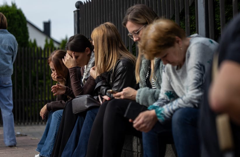 Local residents wait next to the scene where a 15-year-old fatally stabbed the caretaker of his former school and wounded two other adults at the John-Paul II primary school in Leszczydol-Nowiny, Poland, on October 8, 2026, a day after a similar knife attack wounded nine in a Polish high school.