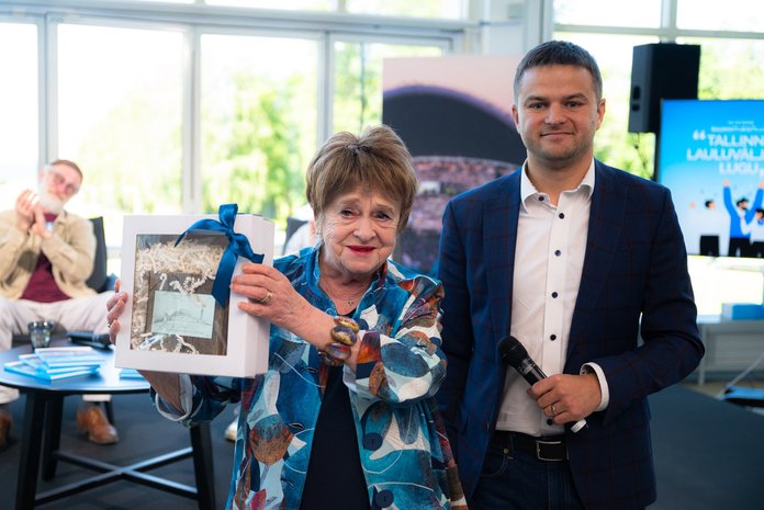 Armastatud luuletaja Leelo Tungal sai raamatuesitlusel Lauluväljaku juhi Urmo Saareoja poolt kingituseks tüki laulukaare originaallaudisest. Taamal aplodeerib koorijuht Raul Talmar.