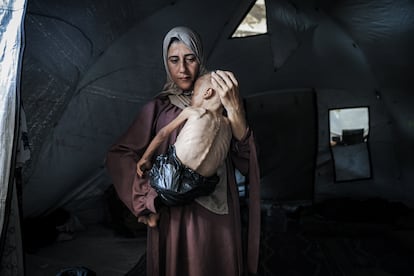 La madre de Muhamad sostiene a su hijo en la tienda de campaña donde viven en la ciudad de Gaza. De pañal, una bolsa de plástico.  