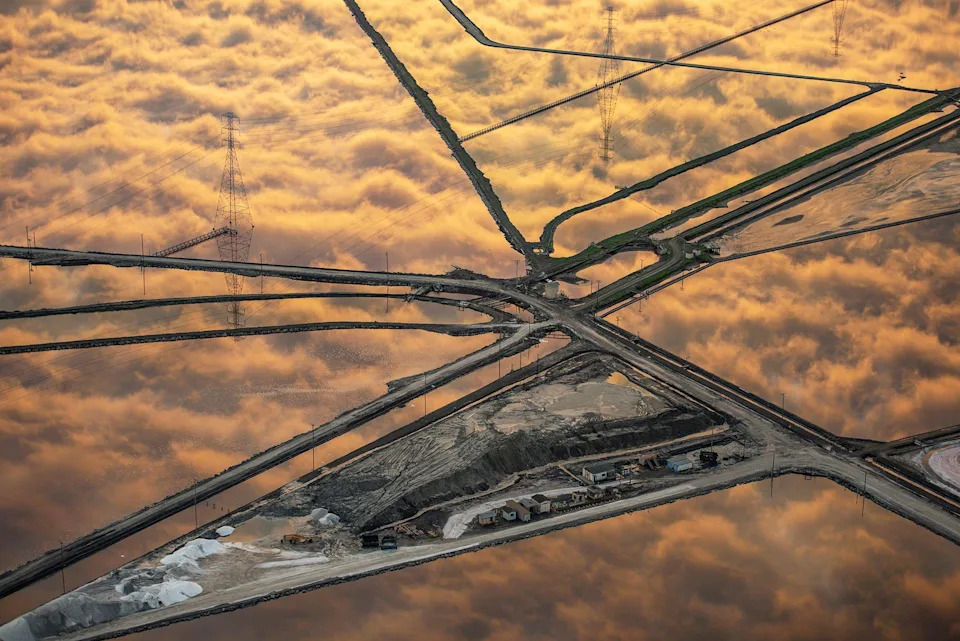 Las nubes doradas se reflejan perfectamente en la cuadrícula de estanques salados. Los estanques se extienden por el paisaje, creando un mosaico de agua resplandeciente y separadores de tierra.
