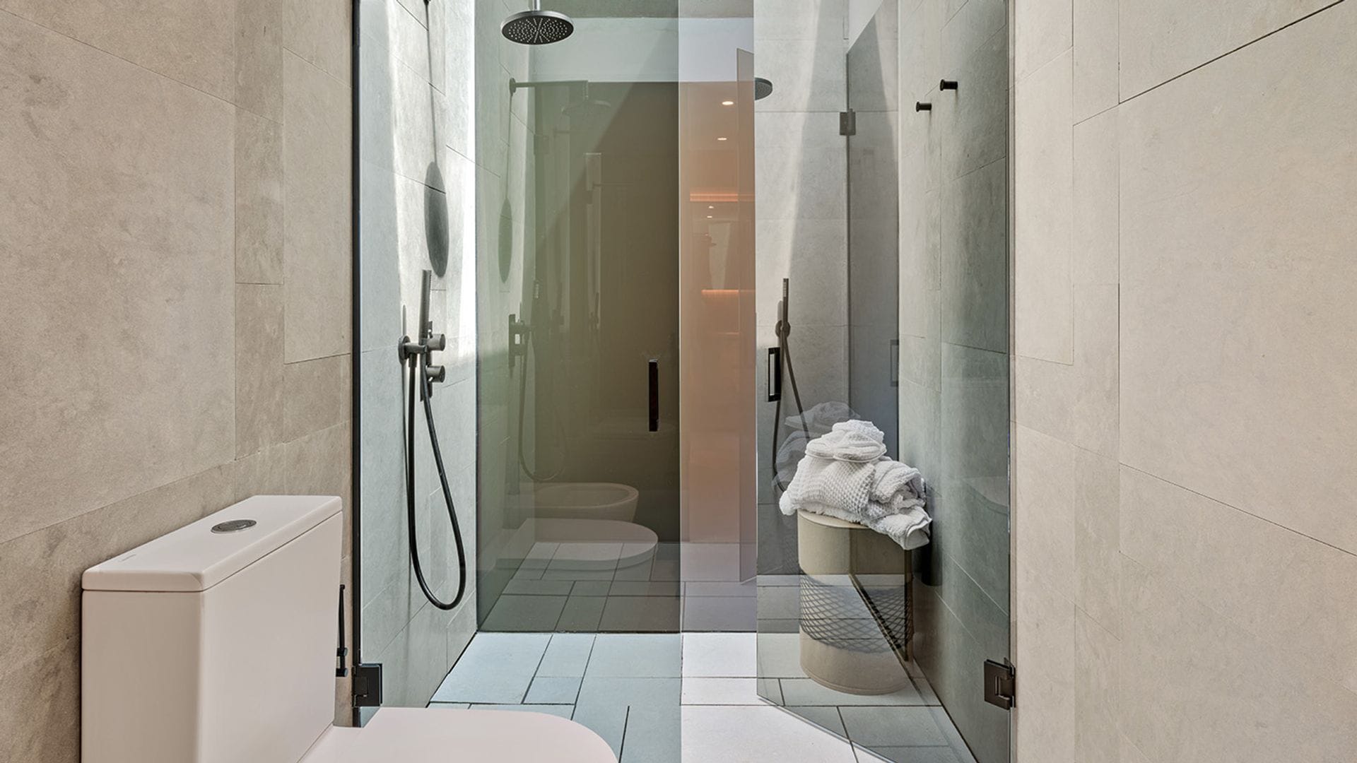 Baño con ducha y mampara, a modo cabina de cristal, con revestimiento blanco y grifería negra