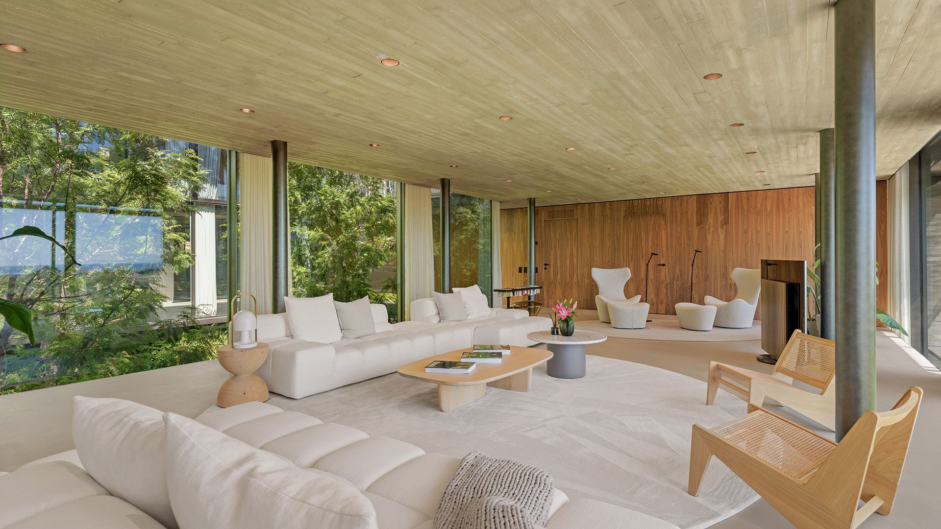 Salón con sofás blancos, alfombra redonda blanca, techo de hormigón, pared de madera, mesa de centro de madera, tabiques de cristal 