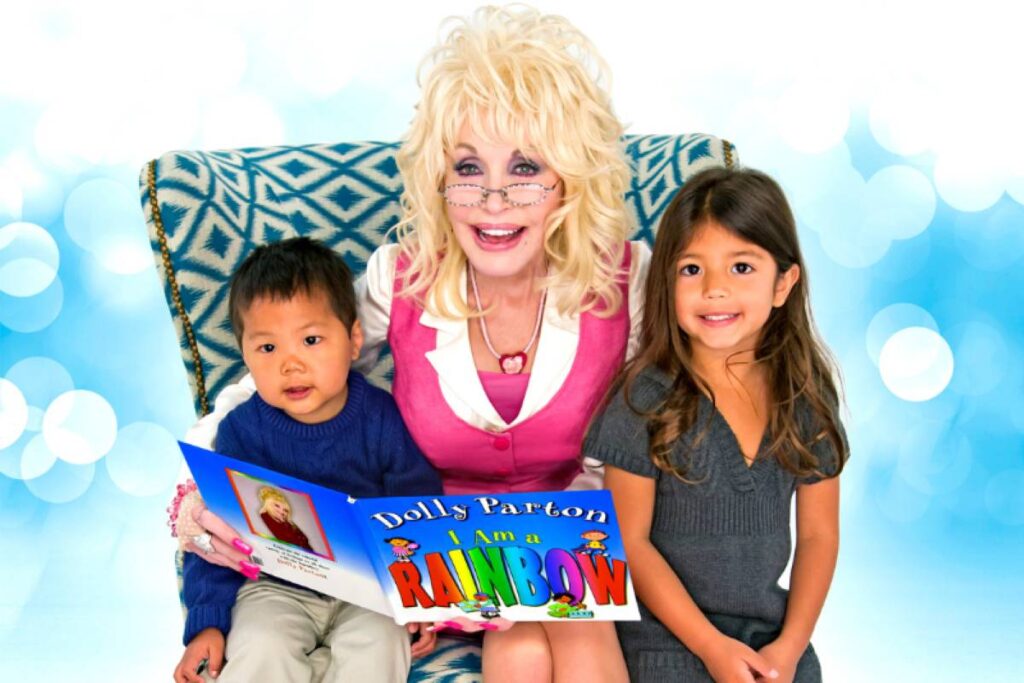 Una imagen de Dolly Parton sentada en un sillón leyendo un libro con dos niños