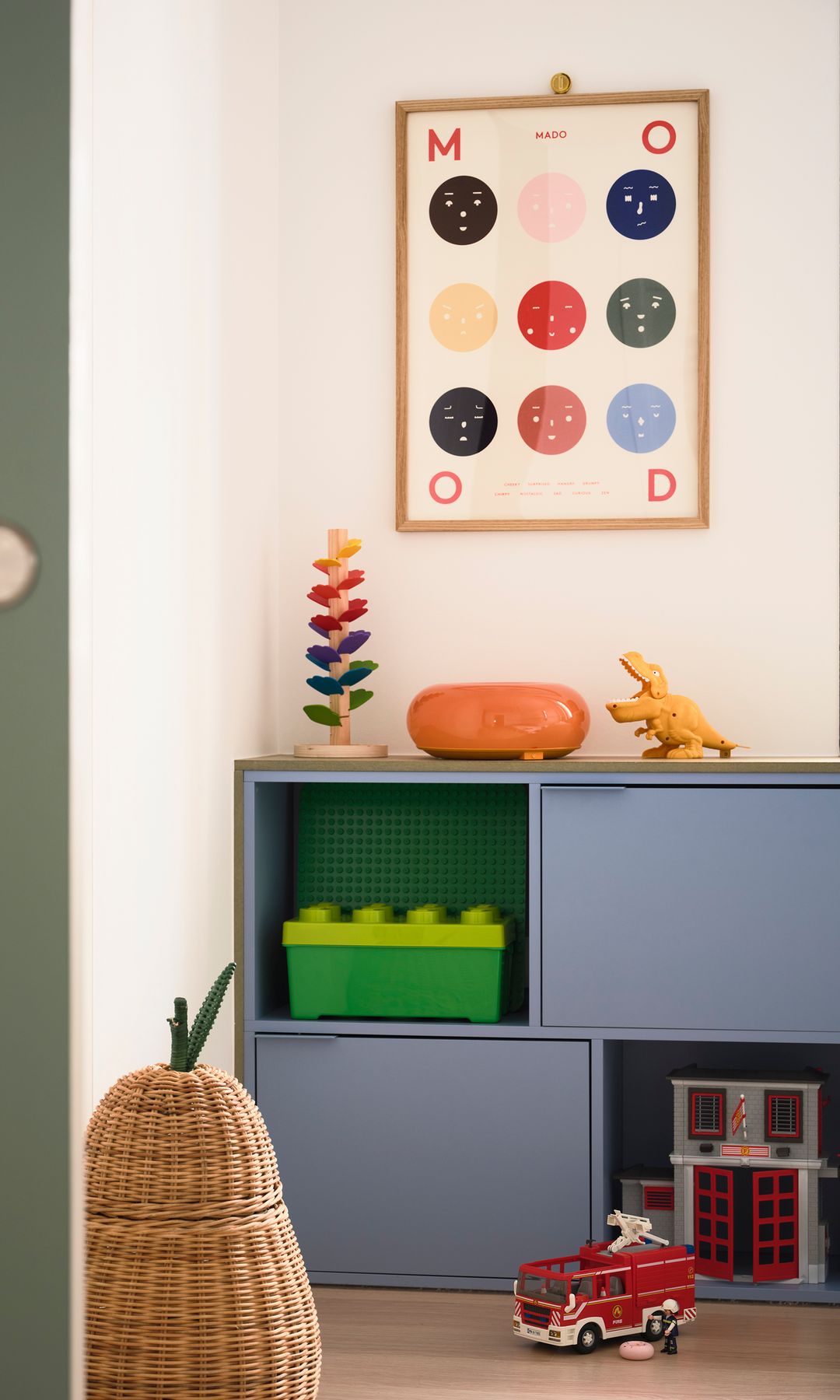 Habitación infantil con estantería azul con cajones, cuadro en la pared, juguetes, cesto para guardar juguetes