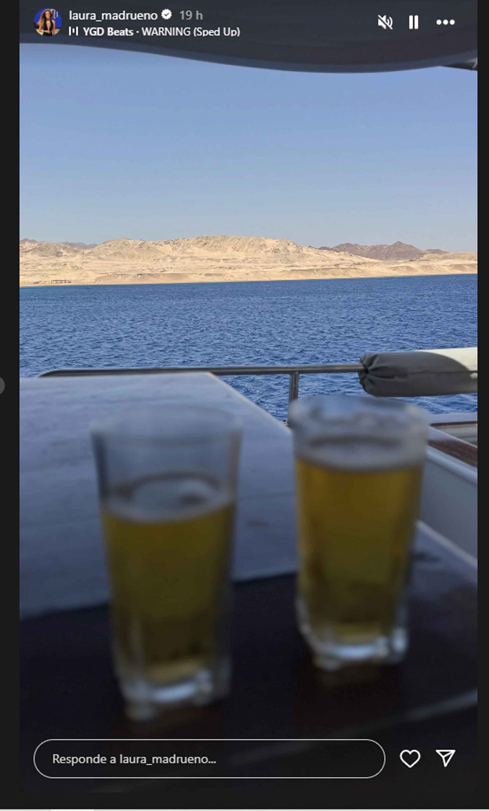two glasses of beer on a table with a view of a body of water and mountains in the background