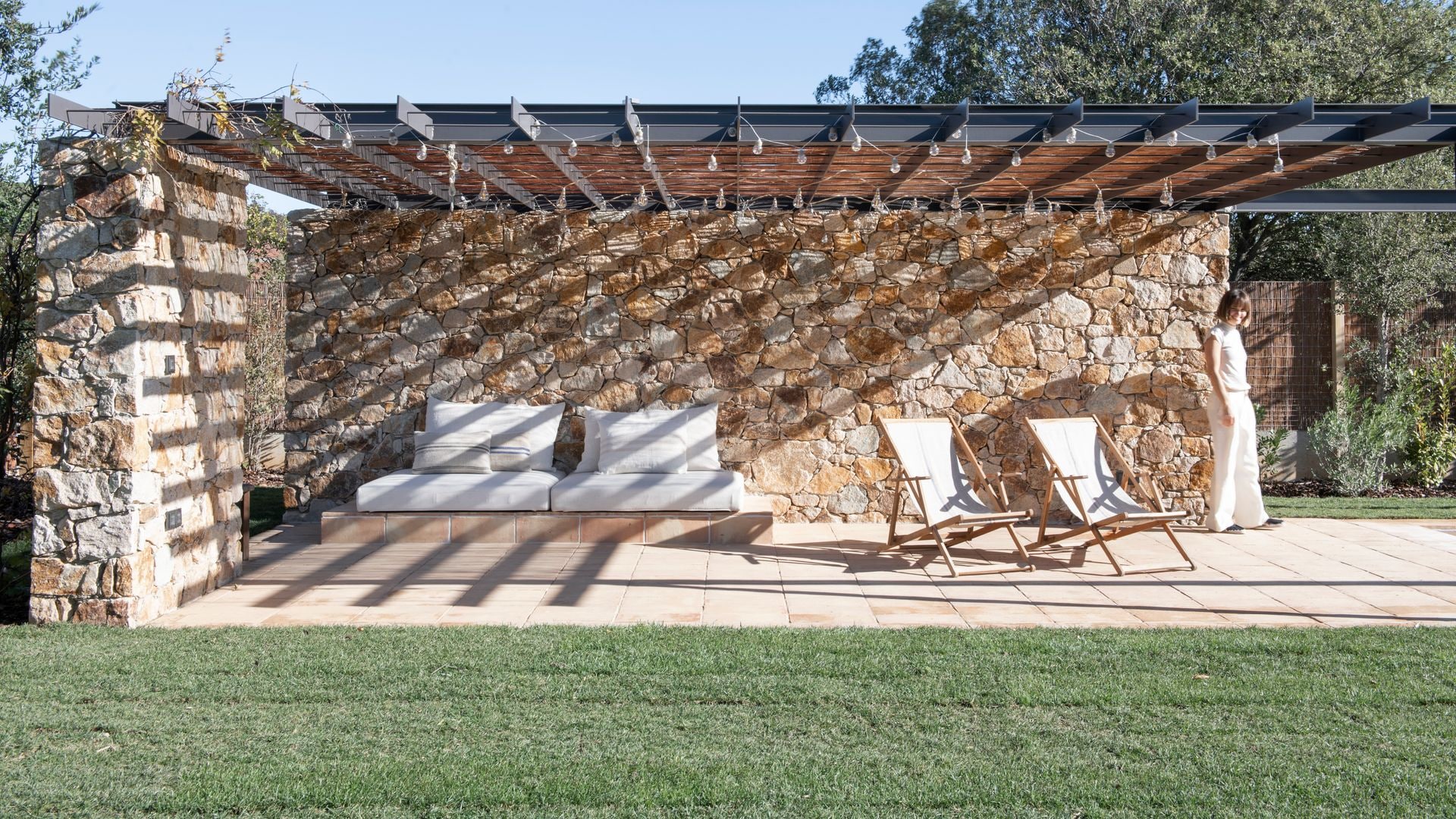 Zona de chill out con camas, tumbonas de lona blanca, mujer, techo de cañizo, suelo de barro, césped