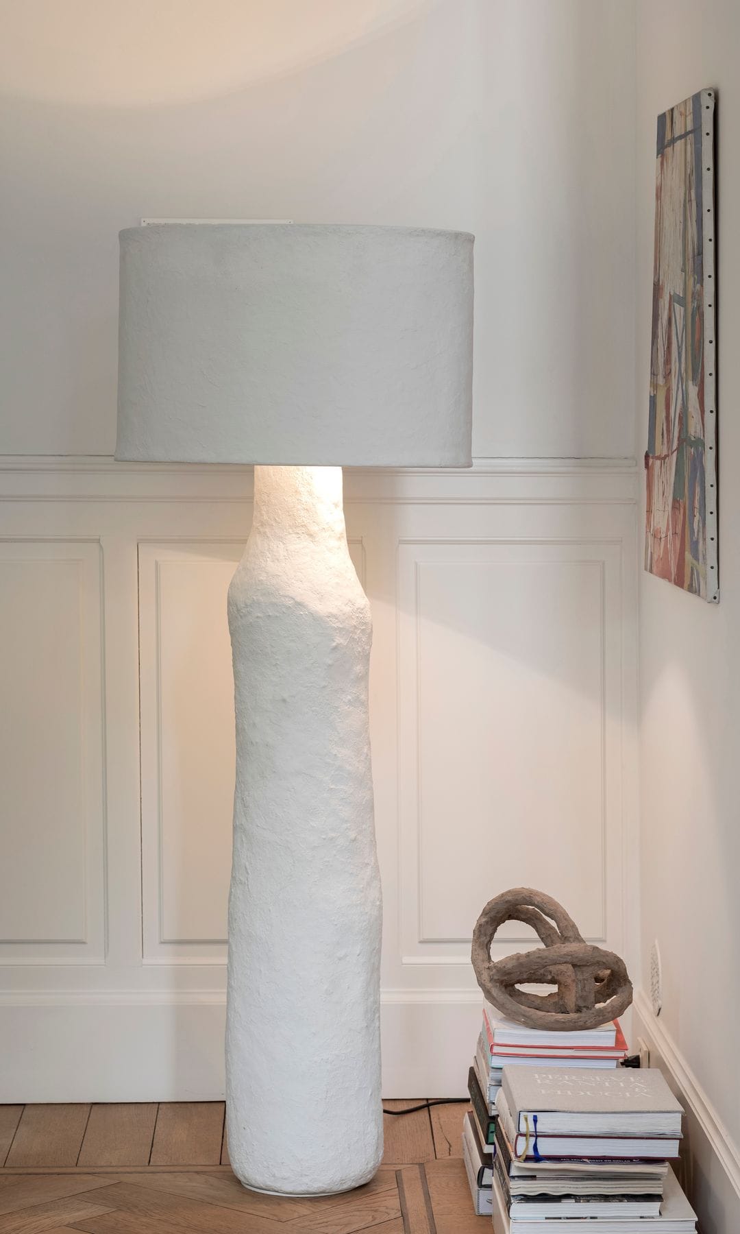 Rincón con friso de madera blanca, lámpara de pie blanca, libros en el suelo