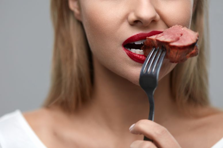 Primer Plano de rostro femenino mordiendo carne
