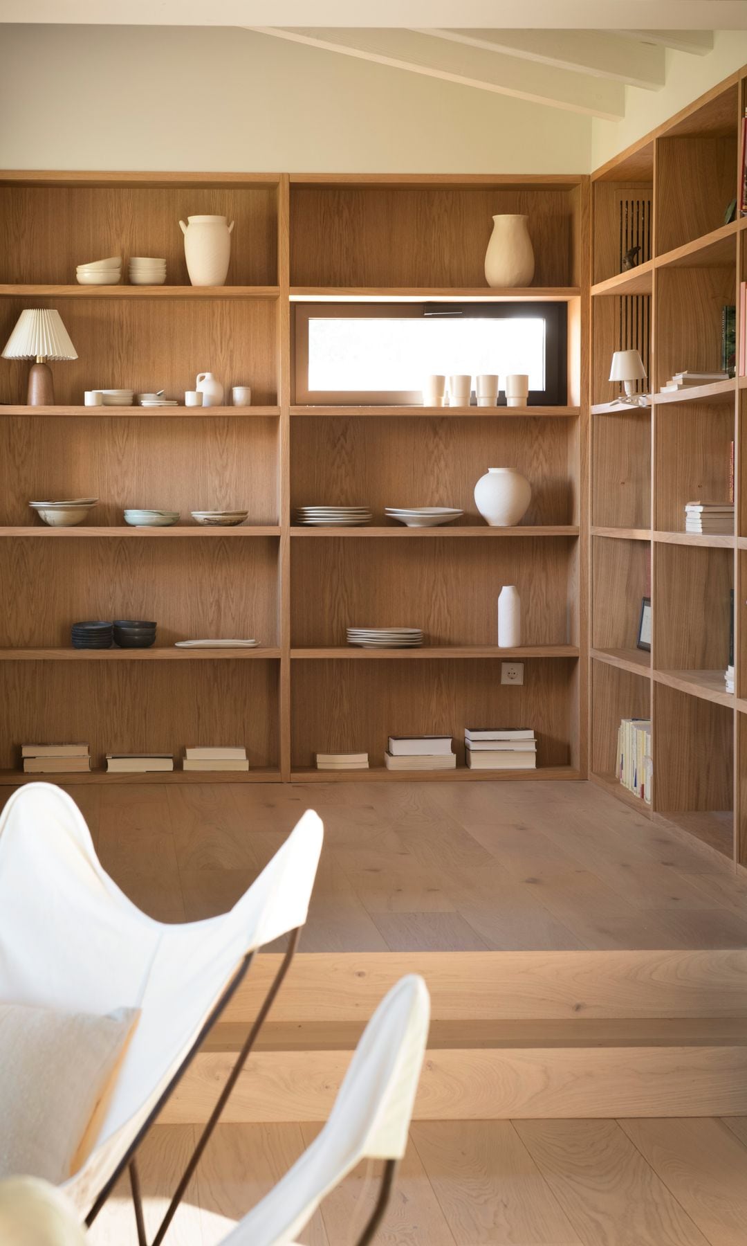 Salón separado en dos zonas mediante dos escalones, librería de madera con trasera con adornos, platos y libros 