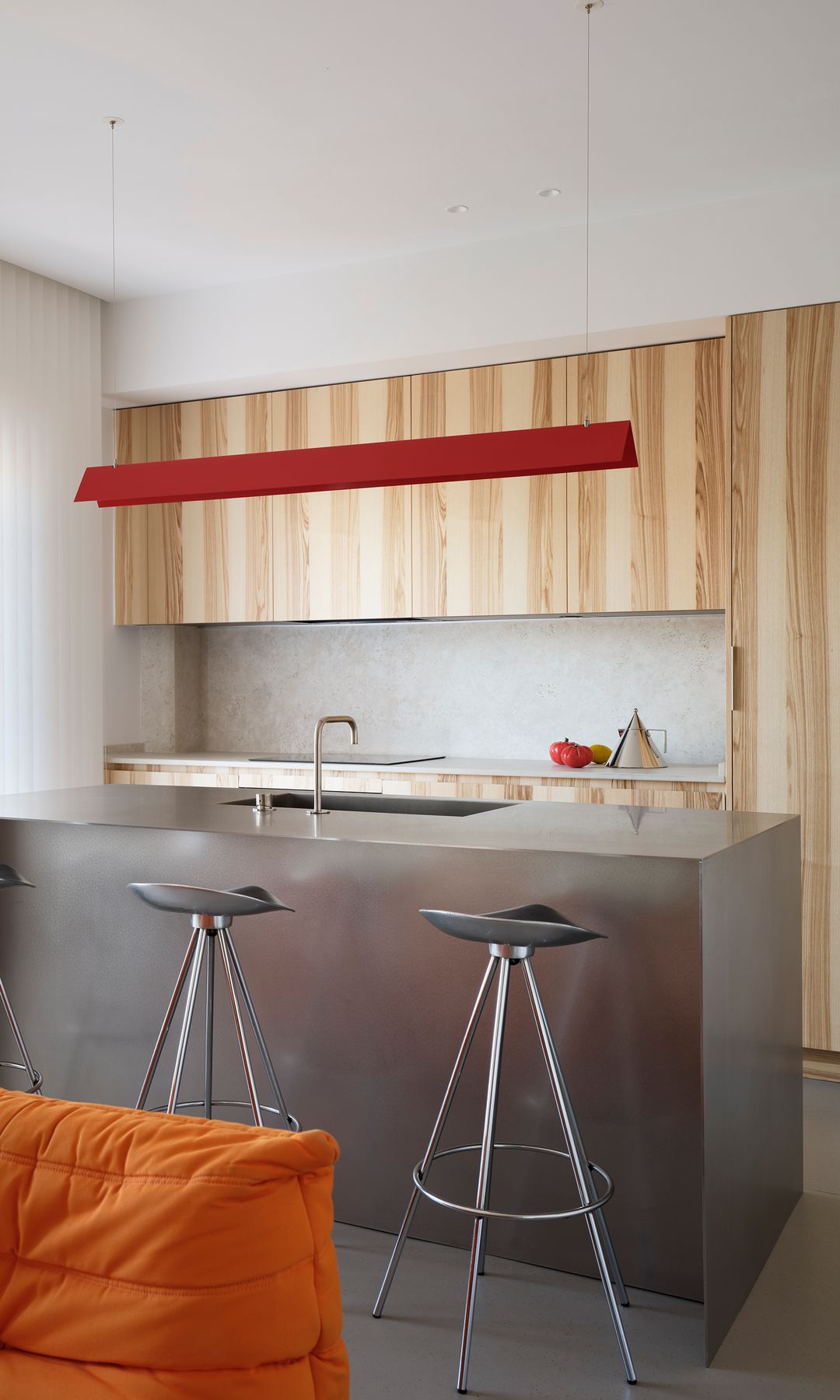 Cocina con isla de acero inoxidable con taburetes altos, muebles de cocina de madera hasta el techo, lámpara de techo sobre la isla de color rojo