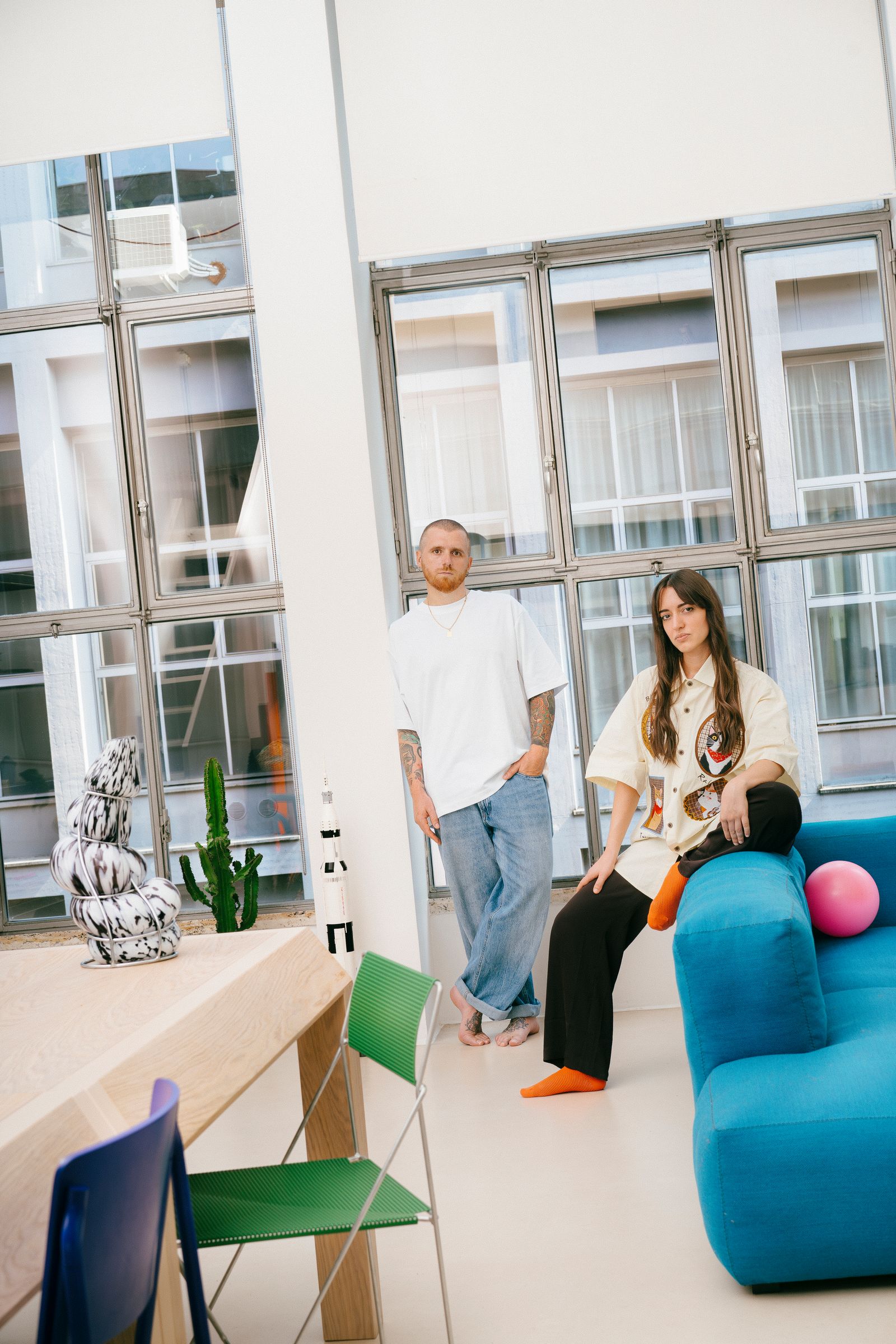 hombre de pie y mujer morena sentada en un sof azul.