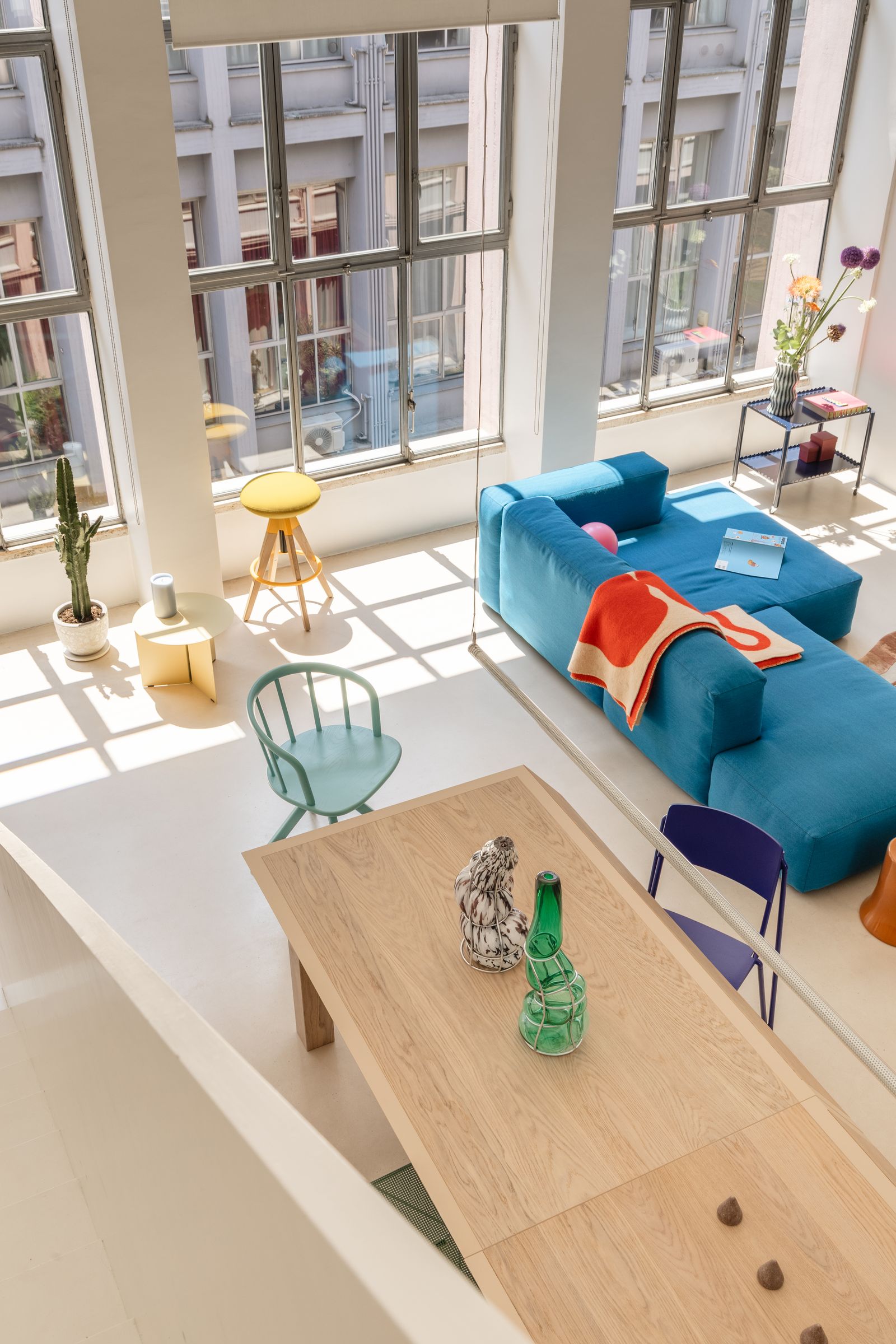 sala con cristalera sof azul taburete amarillo mesa de madera alargada.