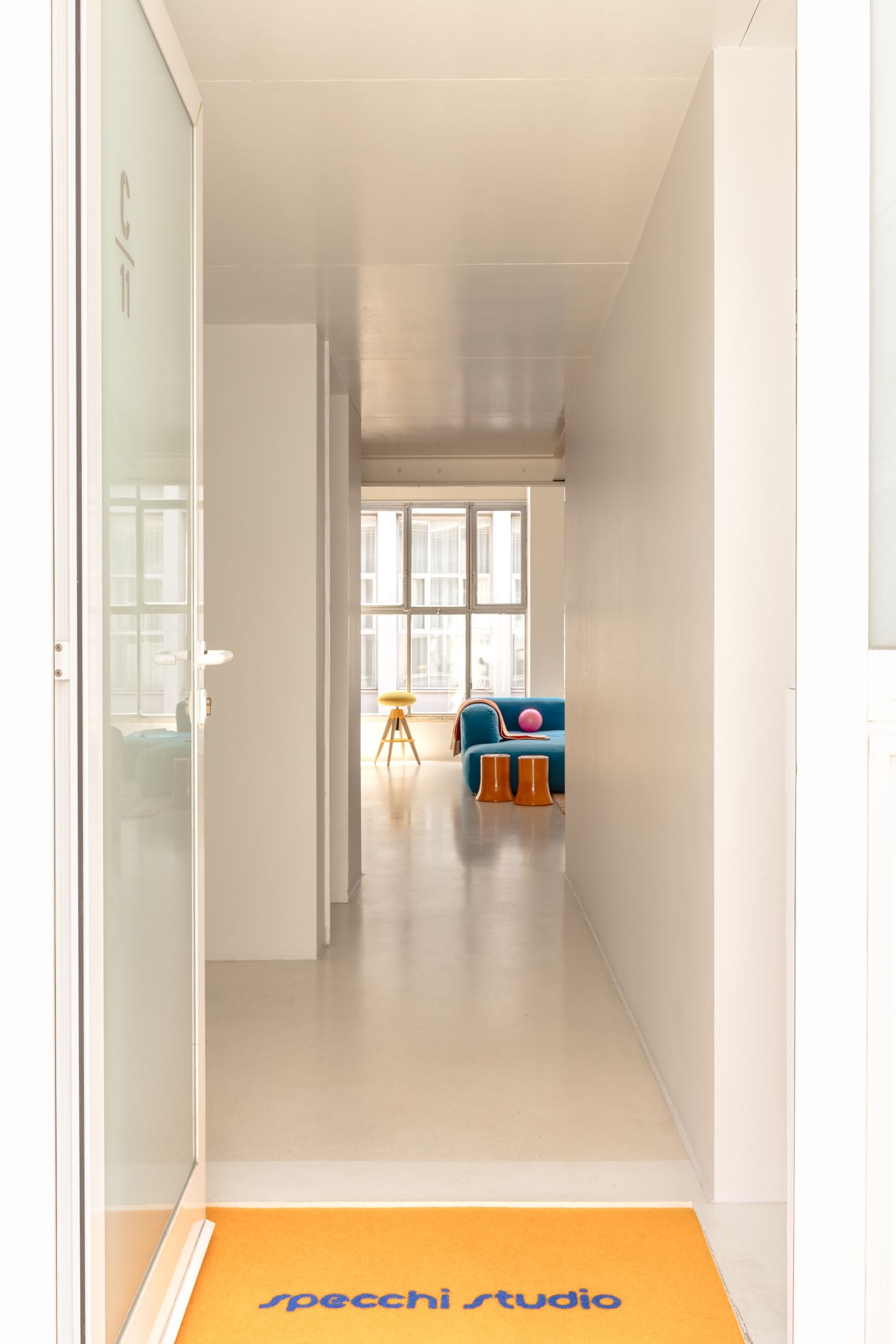 puerta de entrada pasillo blanco taburete amarillo y sof azul.