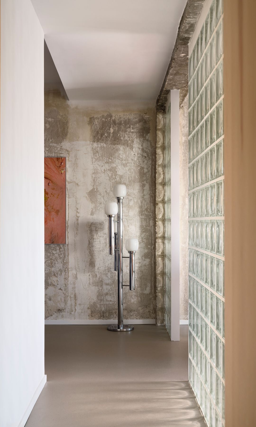 Pasillo con paredes de payés y de yeso, puertas de madera con uñera y lámpara de pie metálica con pantallas blancas