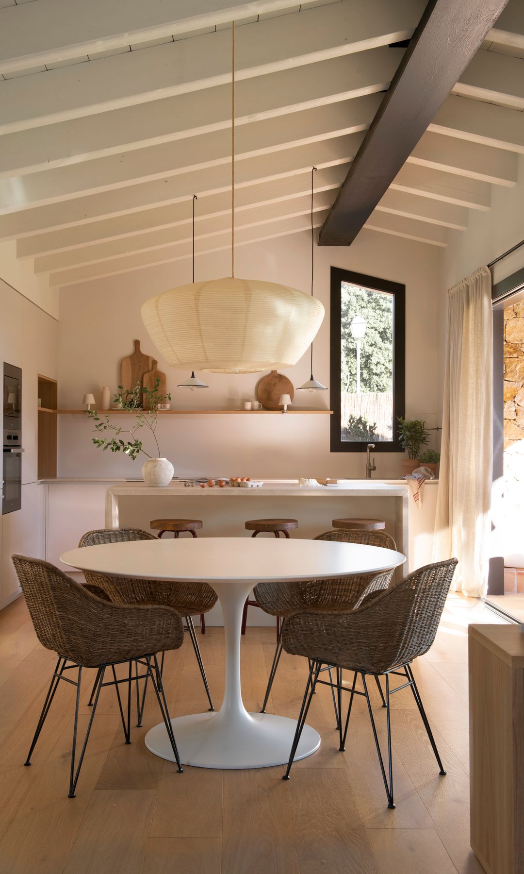 Cocina con comedor con mesa redonda Tulip, sillas de fibras vegetales, lámpara de techo de papel, suelo de madera