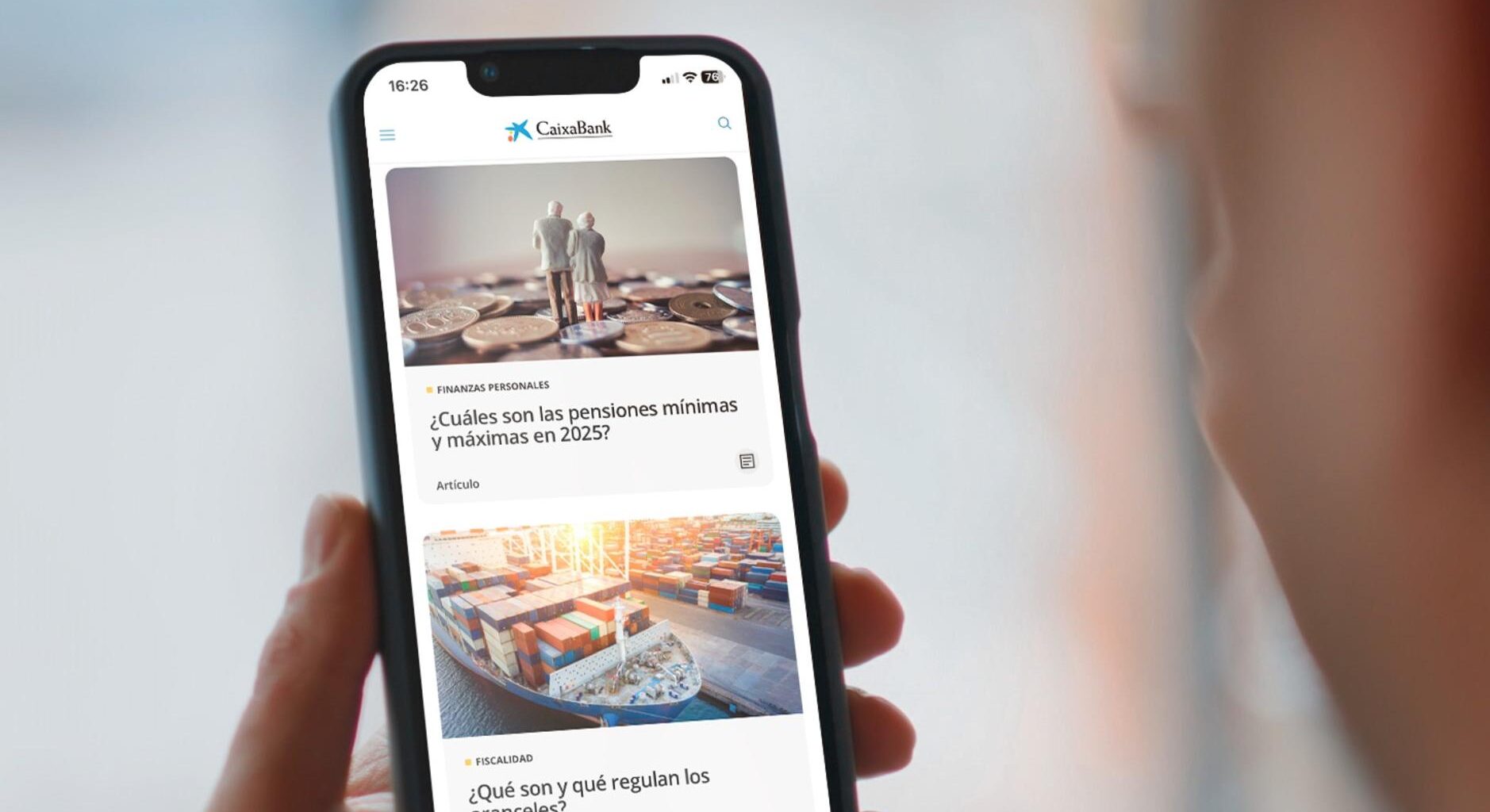 Una persona sujeta un móvil con artículos de CaixaBank