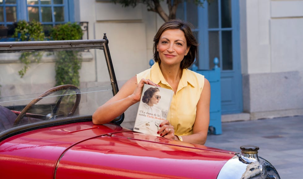 a woman holds a book while leaning on a vintage red car