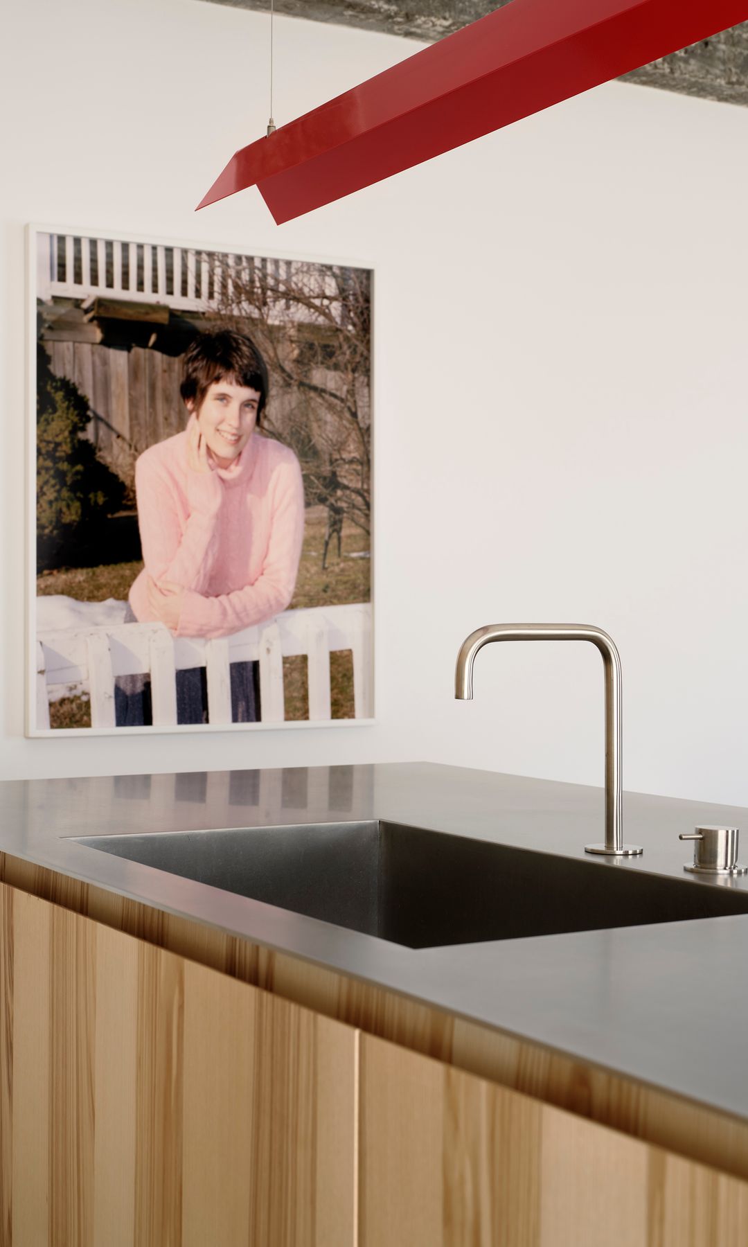 Isla de cocina con la encimera metálica, la estructura de madera de roble, lámpara de techo de color rojo y fotografía en la pared