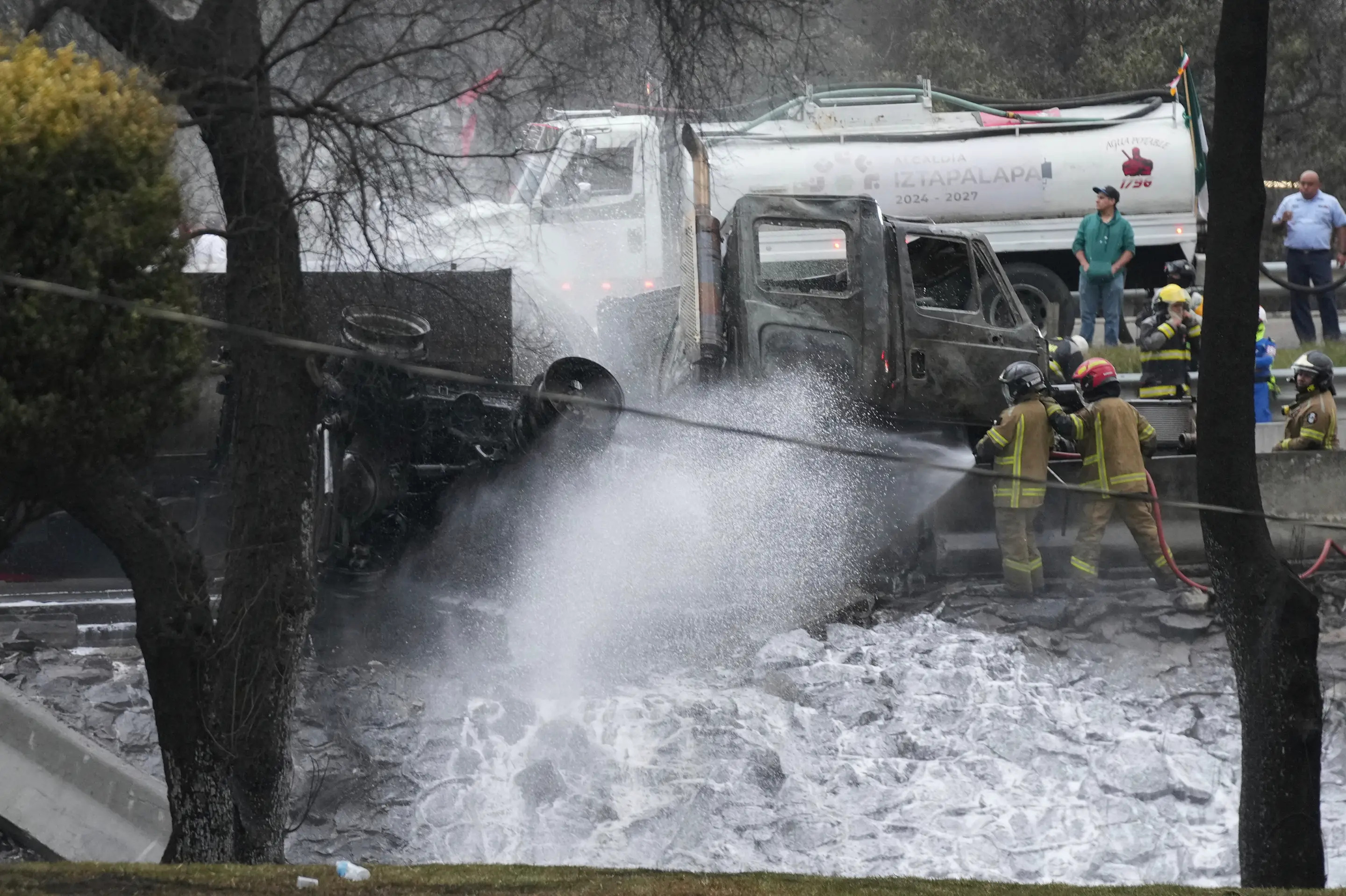 Firefighters spray a hose at a burned car after a gas tanker exploded under a highway underpass in Mexico City, Wednesday, Sept. 10, 2025. (AP Photo/Fernando Llano)