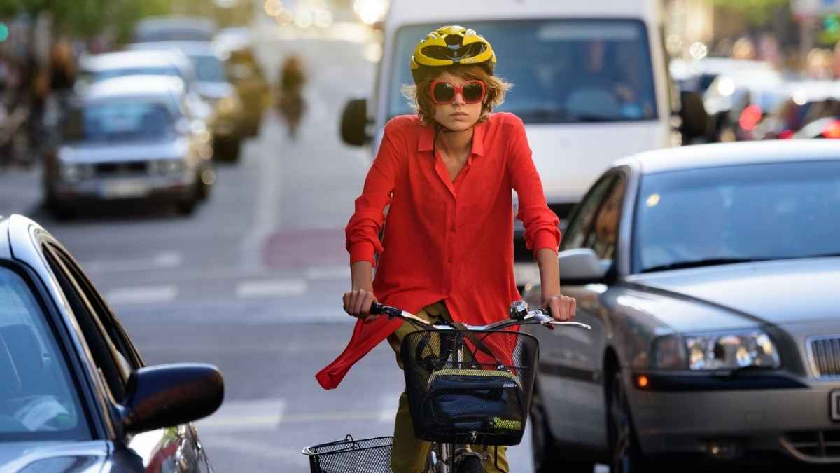 Ciclista con casco circulando en ciudad entre coches con riesgo de dooring al abrirse una puerta inesperadamente
