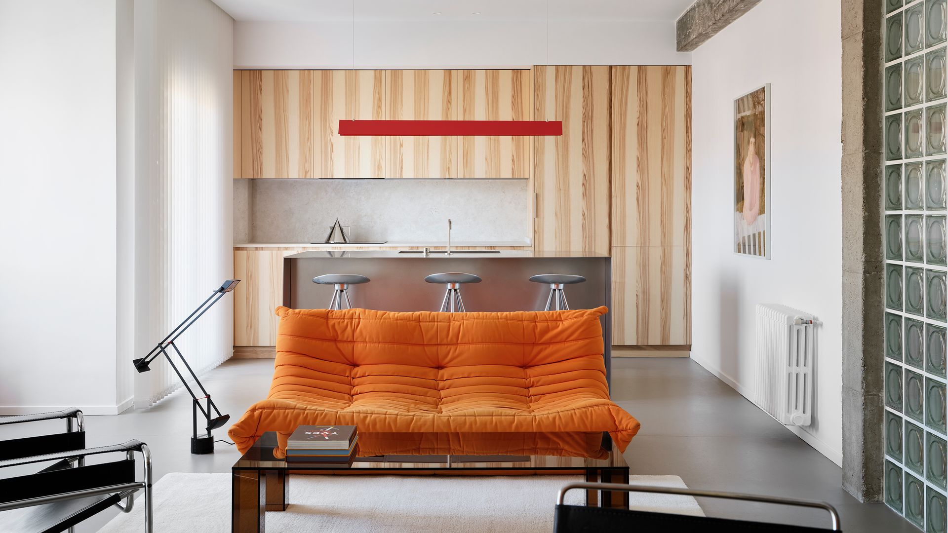 Salón con cocina con sofá de color naranja, isla de cocina, muebles de madera  hasta el techo, fotografía en la pared, lámpara de techo roja