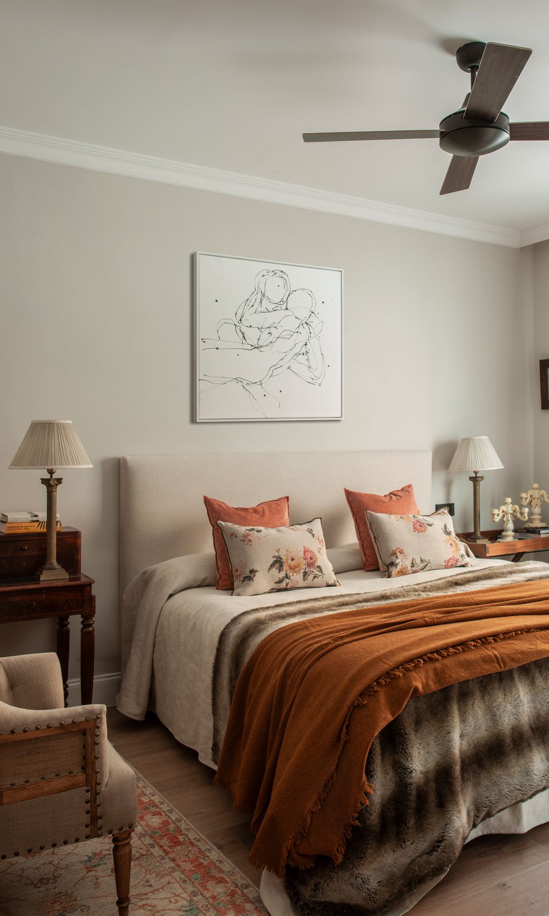 Dormitorio con ventilador en el techo, cabecero tapizado, manta y colcha caldero a los pies de la cama, alfombra, secreter, cuadro en la pared y butaca 