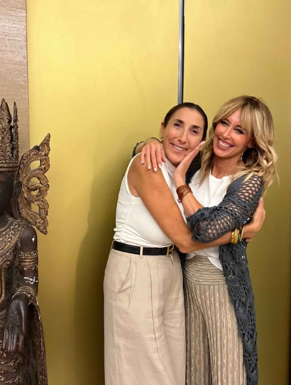 two women embracing in front of a decorative statue
