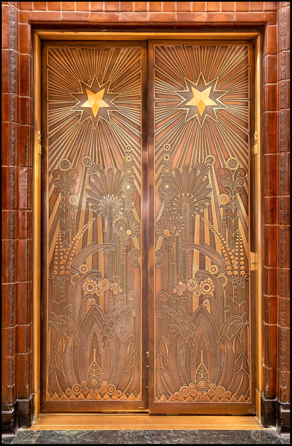 Ornate bronze elevator doors featuring geometric floral and star patterns.