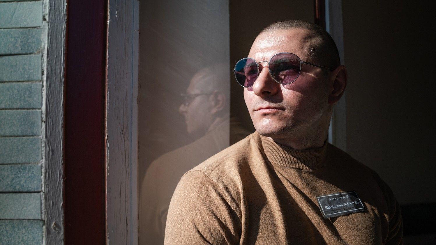 Andrii Askerov, con una camisa marrón y gafas de sol, mira por la ventana de una prisión. 