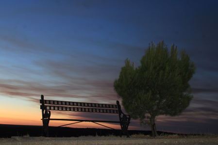 El banco vacío espera bajo el cielo dramático, donde el naranja se rinde ante la inmensidad del azul nocturno.