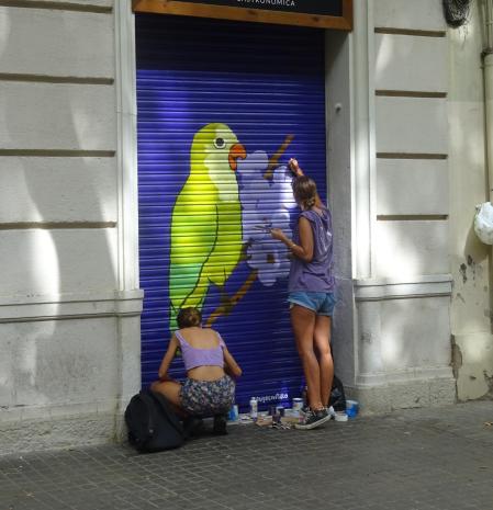 Dos artistas pintan con gusto la persiana de un comercio en la calle Ramon Turró de Barcelona.