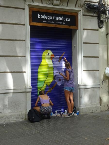 Dos artistas pintan con gusto la persiana de un comercio en la calle Ramon Turró de Barcelona.