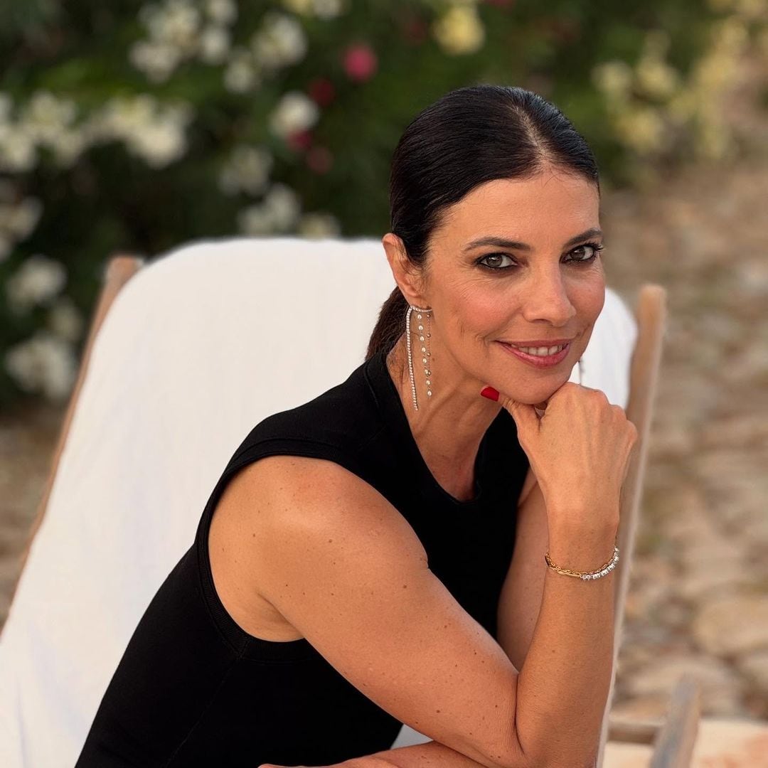 Maribel Verdú en verano de 2025 sentada en una tumbona blanca, con recogido bajo y manicura roja. 