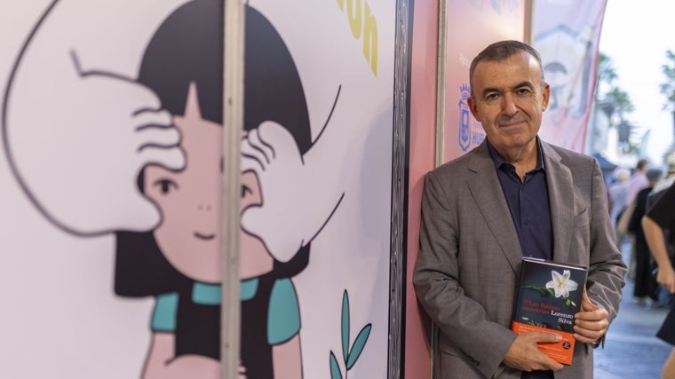 Lorenzo Silva, con su última obra junto a uno de los dibujos del cartel de la Feria del Libro de Huelva de este año