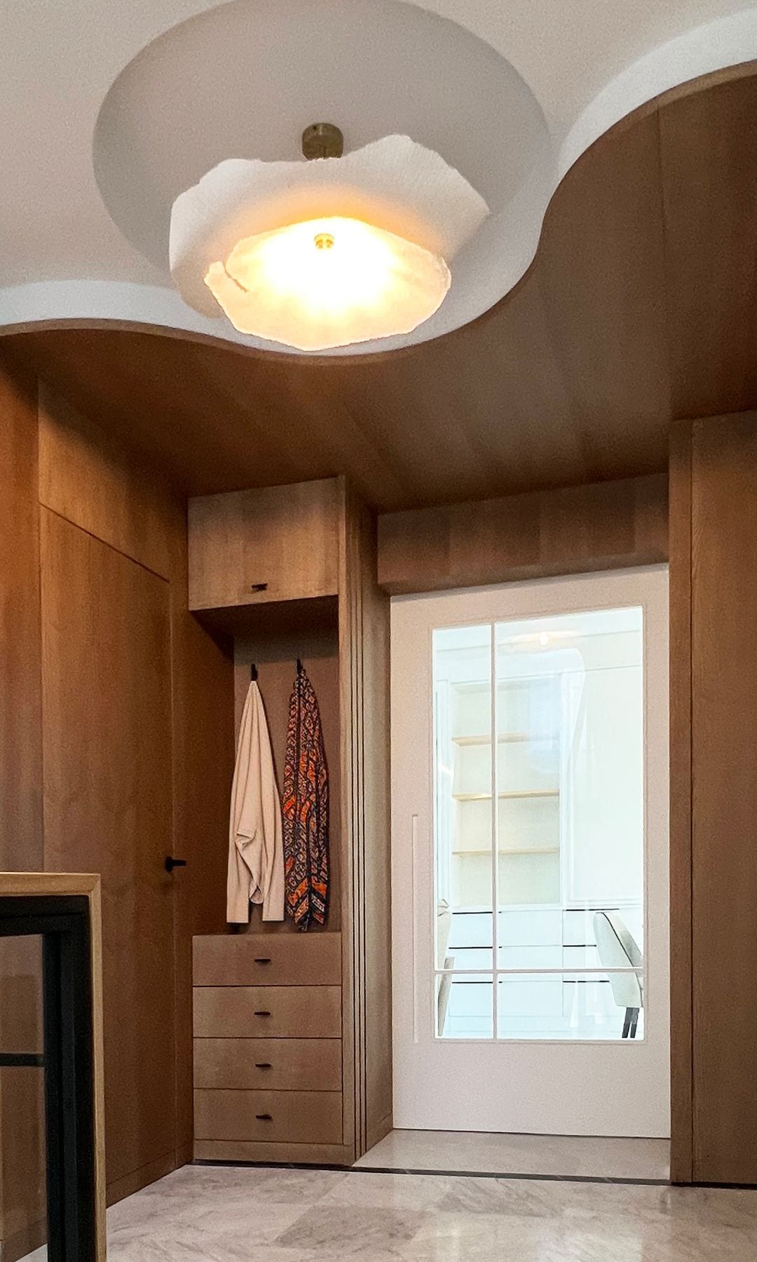 Recibidor con armario abierto con cajones, pared de madera, lámpara de techo y puerta blanca con cristal 