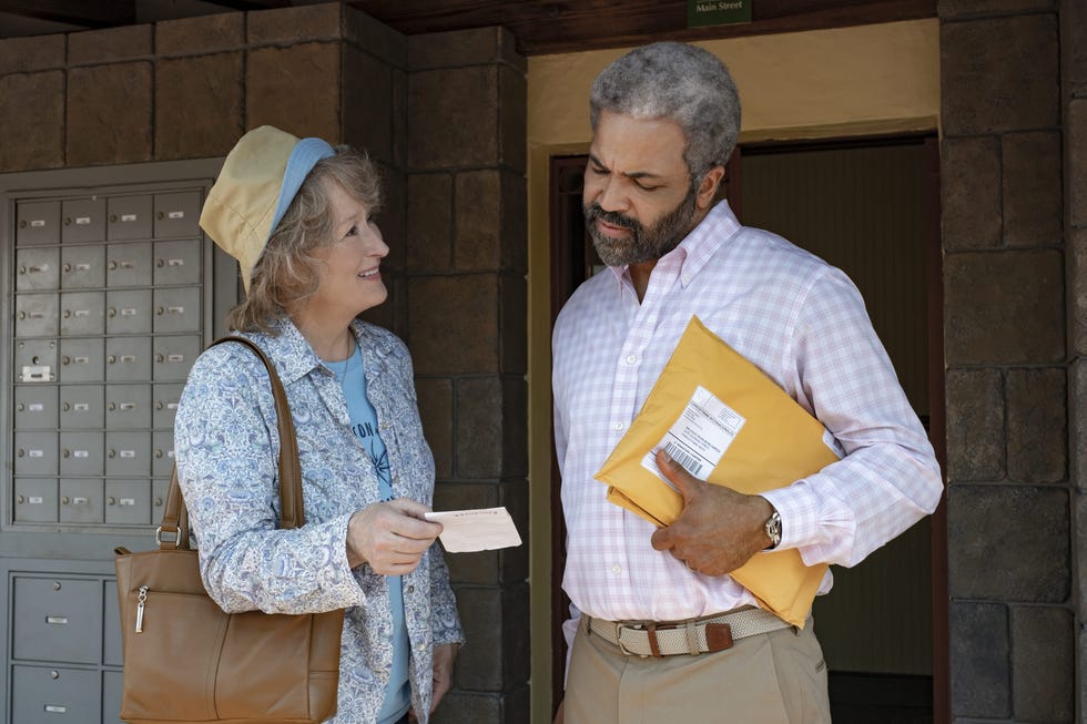 a woman handing over a note to a man holding a package outside a building