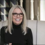 Diane Keaton sonriendo mientras está sentada en un sillón