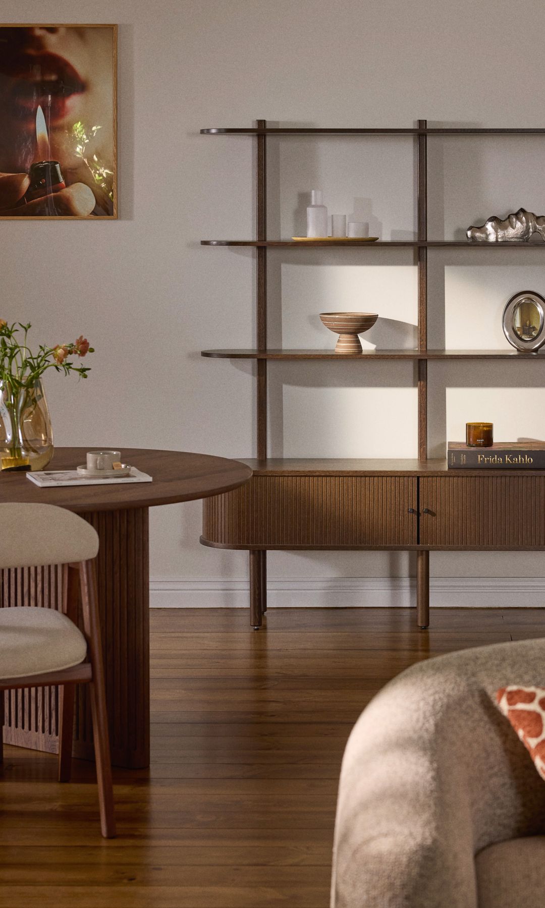 Salón comedor con aparador con estantería, suelo de madera oscuro, sofá beige, cojín, mesa de comedor ovalada de madera, sillas de comedor tapizadas