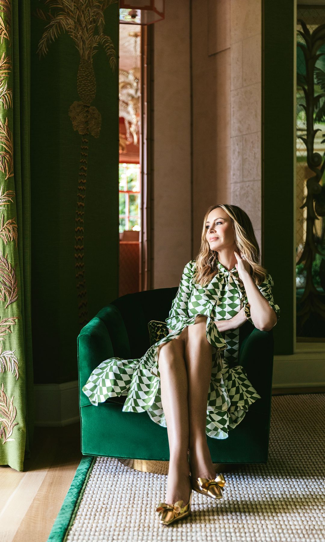 Dee Hilfiger en un sillón verde, vistiendo con estampado verde y blanco y tacones dorados