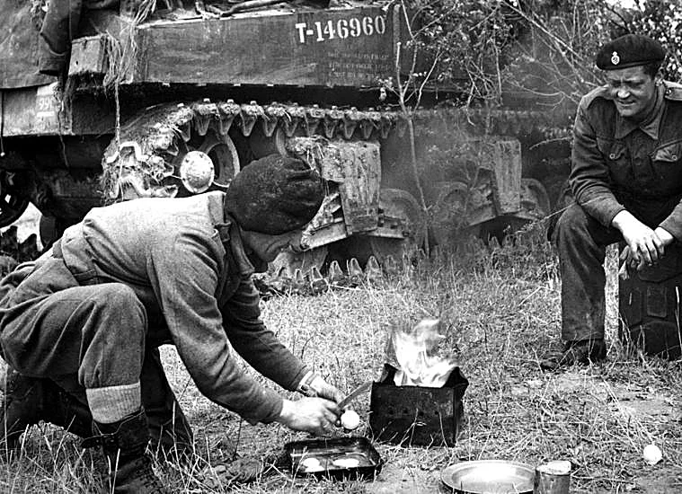 Dos tanquistas preparan la comida frente a un carro de combate