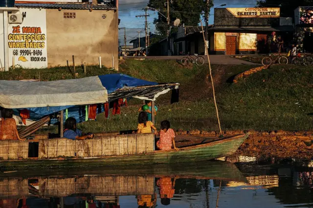 Un grupo de personas, sentadas y de pie en una canoa, que está en la orilla del río Amazonas.
