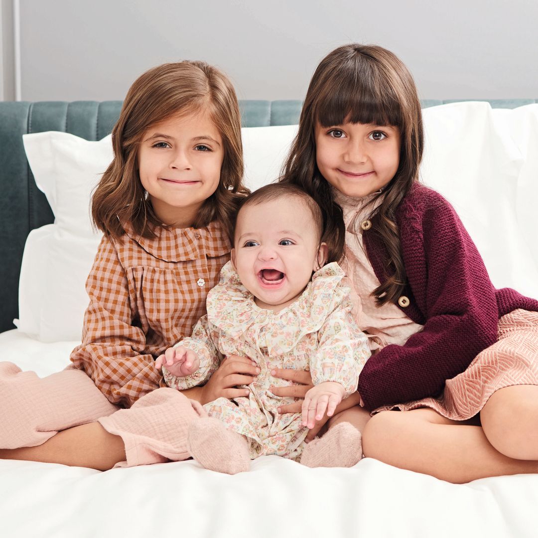Tres niñas sonriendo en una cama, la del medio es un bebé riendo