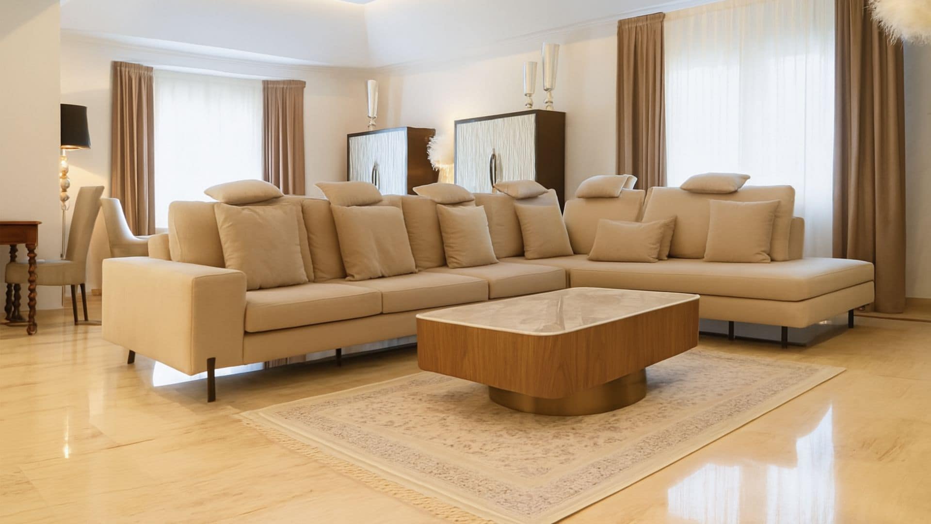 Salón con sofá beige, alfombra, suelo de mármol, mesa de centro, cortinas blancas y marrones, dos armarios con puertas blancas, falso techo con iluminación 