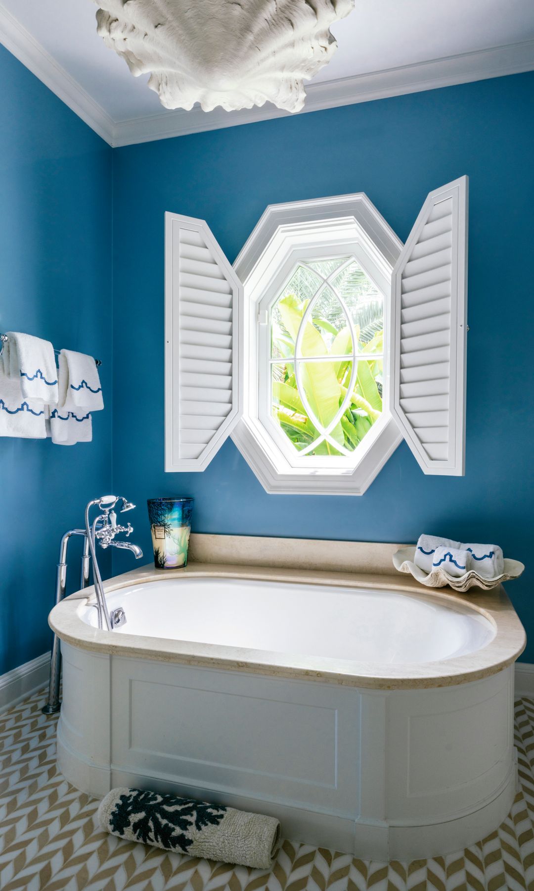 Baño azul con bañera, ventana octogonal, y detalles náuticos con gran lámpara blanca en el techo