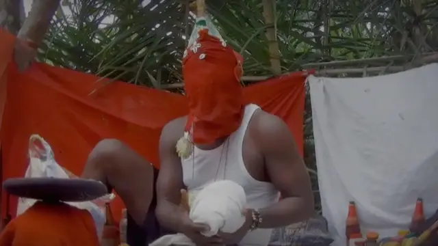 Un hombre que aseguró vender partes humanas, con la cara tapada con una tela ceremonial roja, sostiene algo envuelto en una tela blanca en las manos